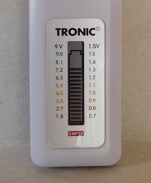 A Tronic analog battery tester with an AAA cell clipped in, its sliding bar sitting in the yellow zone between the 1.2 and 1.1 marks on the 1.5V column, just above a red EMPTY label