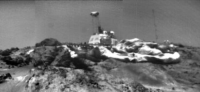 A grainy 1997 photo taken by the Sojourner rover, looking back at the Pathfinder lander on the Martian surface, its camera mast standing up in the middle of the deflated airbags