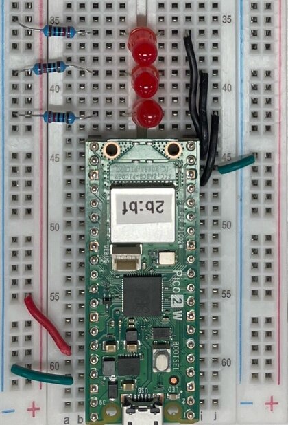 Exemplar 1: a Pico 2 W seated in a breadboard with power and ground wires run to a rail, and three red LEDs each paired with a resistor